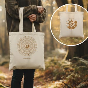 May include: A beige tote bag with a circular, geometric design in brown. The bag has two handles and the words "oraja design" printed at the bottom. A smaller image of the bag is in a circle.