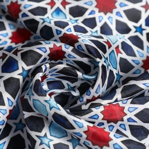 Large mulberry-silk scarf with Islamic geometry and Alhambra-inspired pattern, red border draped over a woman's shoulders.