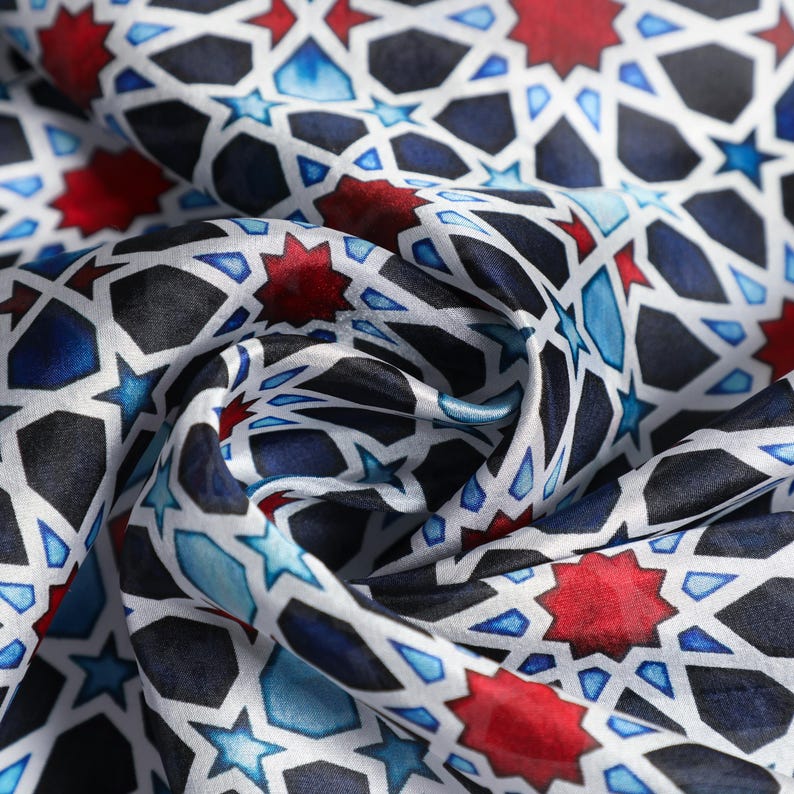 Large mulberry-silk scarf with Islamic geometry and Alhambra-inspired pattern, red border draped over a woman's shoulders.