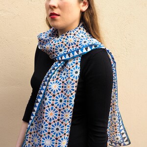 Moroccan tile-inspired silk scarf with blue, white, and orange geometric motifs; large women's neck scarf worn as a wrap.