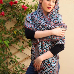 Large mulberry-silk scarf with Islamic geometry and Alhambra-inspired pattern, red border draped over a woman's shoulders.