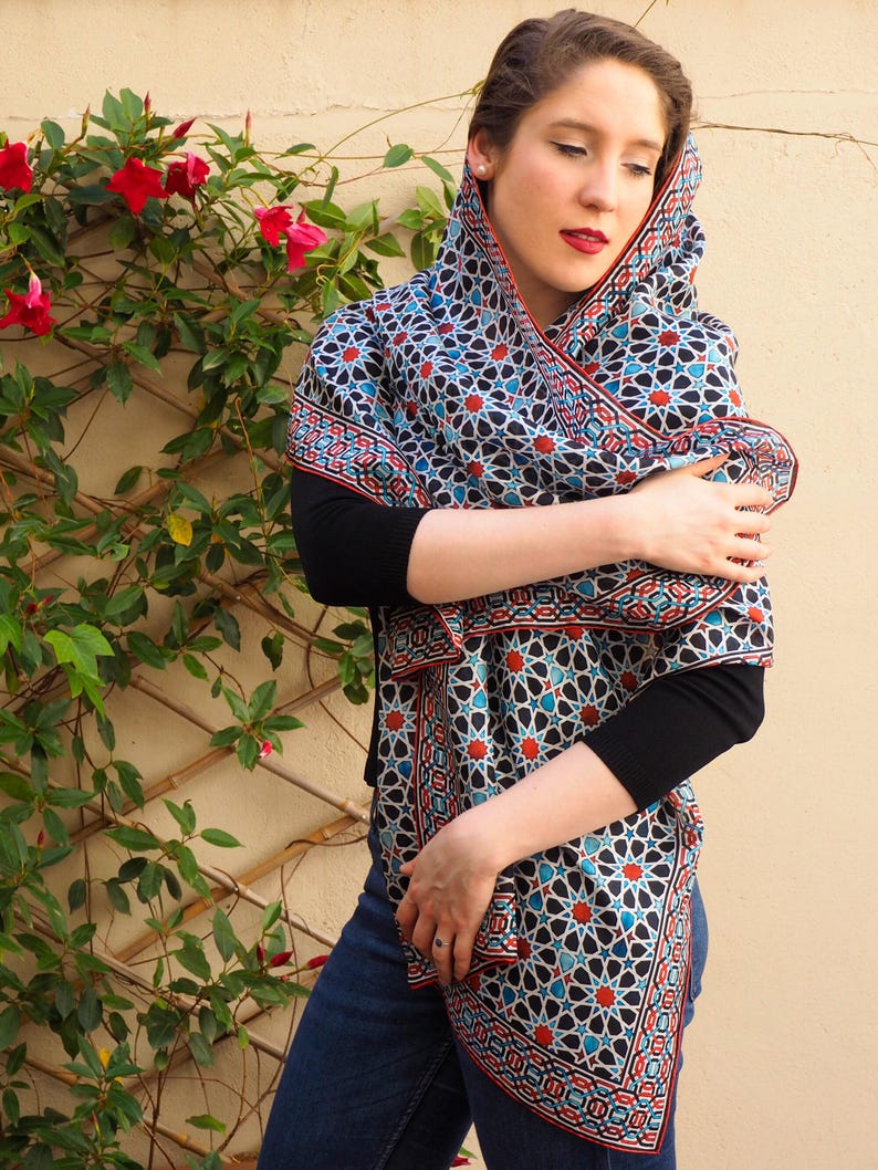 Large mulberry-silk scarf with Islamic geometry and Alhambra-inspired pattern, red border draped over a woman's shoulders.