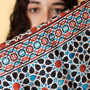 Large mulberry-silk scarf with Islamic geometry and Alhambra-inspired pattern, red border draped over a woman's shoulders.