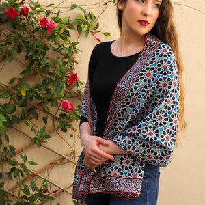 Large mulberry-silk scarf with Islamic geometry and Alhambra-inspired pattern, red border draped over a woman's shoulders.
