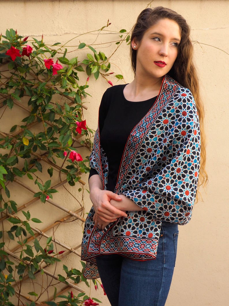 Large mulberry-silk scarf with Islamic geometry and Alhambra-inspired pattern, red border draped over a woman's shoulders.