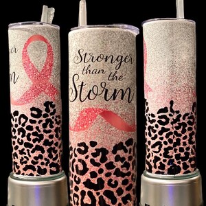 May include: Three pink and black leopard print tumblers with pink glitter and a pink ribbon. The center tumbler has the text "Stronger than the Storm" in black.