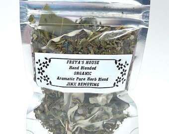 May include: A clear, resealable bag filled with a blend of dried herbs. The bag has a white label with the text "FREYA'S HOUSE Hand Blended ORGANIC Aromatic Pure Herb Blend JINX REMOVING". The herbs are a mix of green and brown.