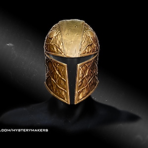 May include: A gold-colored helmet with a textured surface and a diamond pattern on the lower portion. The helmet has a visor and is set against a black background. The text "PATREON.COM/MYSTERYMAKERS" is visible in the lower left corner.