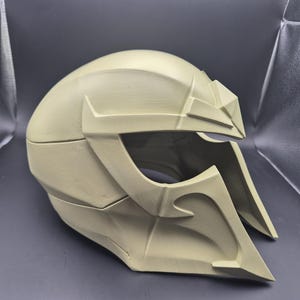 Peut inclure: Un casque beige avec un design futuriste. Le casque présente des formes angulaires, une ouverture pour la visière et des éléments décoratifs sur le dessus et les côtés. L'esthétique générale suggère un thème de science-fiction ou de cosplay.