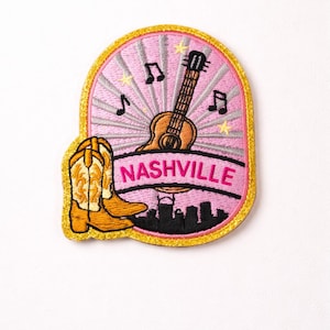 May include: Embroidered patch featuring a pink background with a guitar, musical notes, and stars. A pair of cowboy boots and the word "NASHVILLE" are also included. The patch has a gold border.