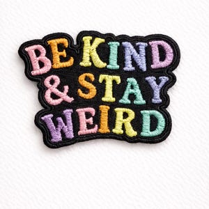 May include: Embroidered patch with the words "BE KIND & STAY WEIRD" in colorful, stitched lettering. The patch has a black border and the text is in pink, yellow, green, orange, and purple. The patch is on a white background.