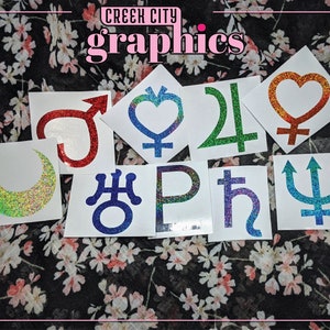 May include: Nine glitter stickers featuring various astrological symbols, including the moon, sun, Venus, Mars, Jupiter, Saturn, Uranus, Neptune, and Pluto. The stickers are on a white background and have a holographic finish.