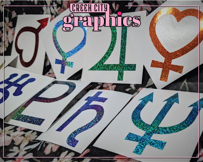 May include: A collection of holographic vinyl stickers featuring various symbols and designs, including hearts, planets, and astrological signs. The stickers are on a white background and have a glittery finish. The text "Creek City Graphics" is visible at the top of the image.