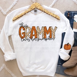 May include: White sweatshirt with the text "this grammy loves her pumpkin" in orange and brown letters with a leopard print pattern. A small orange pumpkin is in the bottom right corner of the image.