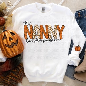 May include: White sweatshirt with the text "This Nanny loves her pumpkin" in orange and brown leopard print letters.