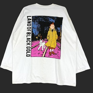 Puede incluir: Camiseta blanca de manga larga con un gr&aacute;fico del c&oacute;mic "Land of Black Gold". El gr&aacute;fico muestra un personaje con un abrigo amarillo con un perro blanco caminando sobre un camino rosa. El texto "LAND OF BLACK GOLD" est&aacute; impreso verticalmente.