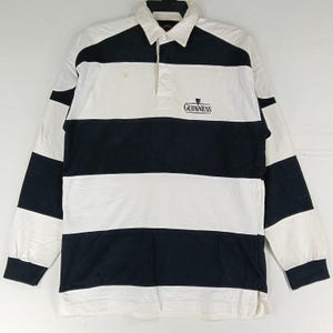 May include: A long-sleeved rugby shirt with alternating white and navy blue horizontal stripes. The shirt features a white collar and a three-button placket. The Guinness logo is embroidered on the chest.