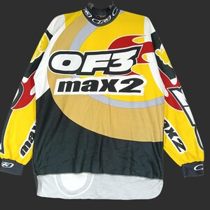 May include: A long-sleeved jersey with a high collar, featuring a bold design in yellow, black, white, and red. The jersey has the text "OF3 max2" prominently displayed on the front. The sleeves have additional graphics and text.