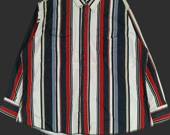 May include: A long-sleeved shirt with a vertical stripe pattern in red, black, white, and grey. The shirt features two chest pockets and a classic collar. The Wrangler brand name is visible on the collar.
