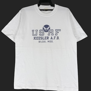 May include: White t-shirt with a crew neck and short sleeves. The front features the text "USAF" above "KEESLER A.F.B. BILIXI, MISS." in navy blue. A navy blue emblem is centered above the text. The shirt is made of a soft material.