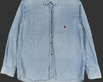 May include: Light blue denim button-down shirt with long sleeves. Features a button-down collar and a small red logo on the chest. The shirt has a classic fit and is made of a durable denim fabric.