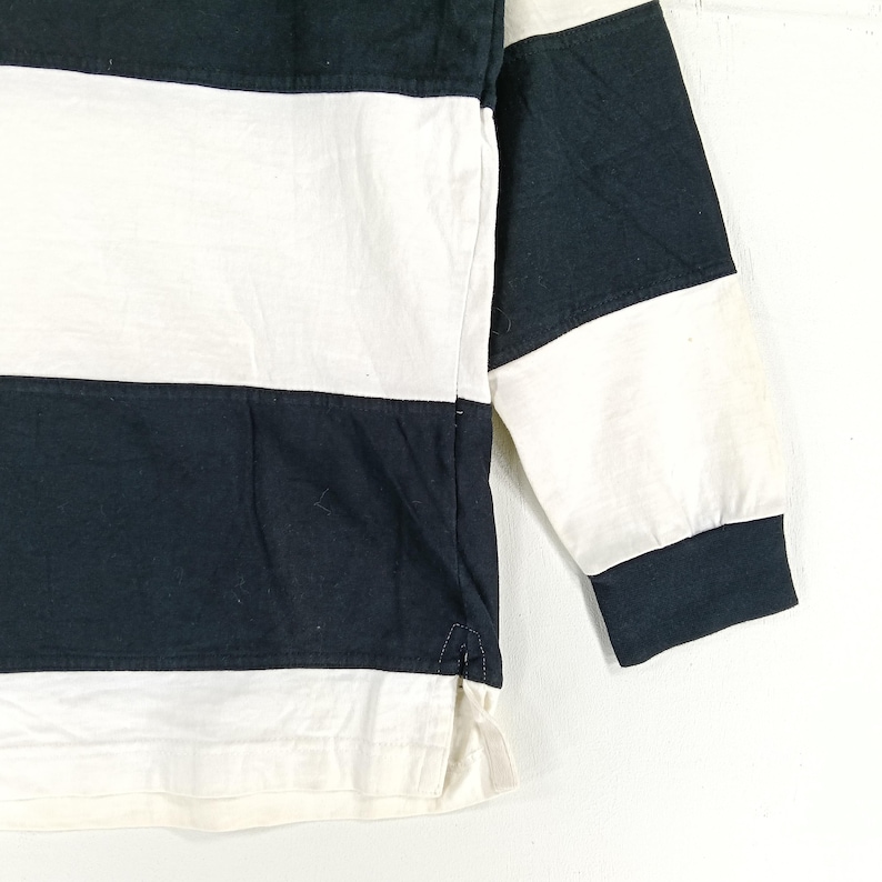 May include: Close-up of a long-sleeved shirt with alternating horizontal stripes of black and white. The sleeve cuff and collar are solid black. The shirt is made of a soft, likely cotton, material.