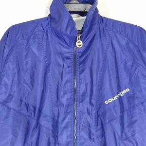 May include: A royal blue Courr&egrave;ges zip-up jacket. The jacket has a high collar and a silver zipper. The Courr&egrave;ges logo is printed in white on the front. The jacket is made of a lightweight, possibly nylon, material.
