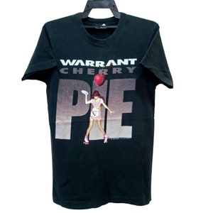 Könnte beinhalten: Schwarzes T-Shirt mit einem grafischen Aufdruck einer Frau auf Rollschuhen, die eine Kirsch-Torte hält. Der Text "WARRANT CHERRY PIE" ist auf dem Shirt aufgedruckt.
