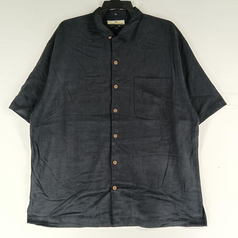Peut inclure: Chemise bleu marine fonc&eacute; &agrave; manches courtes avec boutons et une poche poitrine. Le col est classique et les boutons sont en bois. Le tissu semble &ecirc;tre doux et textur&eacute;.