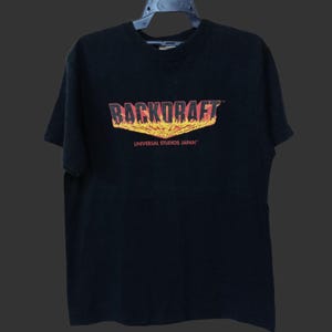 May include: Black t-shirt with the word "BACKDRAFT" in red and orange, with a flame design. Below the word is the text "UNIVERSAL STUDIOS JAPAN" in white. The shirt has short sleeves and a crew neck.
