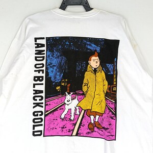 Puede incluir: Camiseta blanca de manga larga con un gr&aacute;fico del c&oacute;mic "Land of Black Gold". El dise&ntilde;o muestra un personaje con un abrigo amarillo con un perro blanco caminando por un camino rosa y morado.