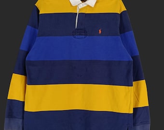 Könnte beinhalten: Ein langärmeliges Rugby-Shirt mit horizontalen Streifen in Marineblau, Gelb und Königsblau. Das Shirt hat einen weißen Kragen, eine Knopfleiste mit drei Knöpfen und ein kleines rotes Logo auf der Brust.