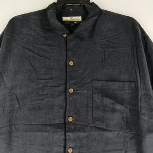 Peut inclure: Une chemise boutonn&eacute;e bleu marine fonc&eacute; avec une poche poitrine unique. La chemise a un col et des boutons de couleur bois. Le nom de la marque est visible sur l'&eacute;tiquette.