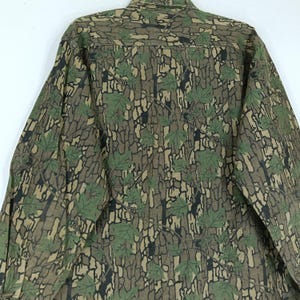 May include: A long-sleeved button-down shirt with a camouflage pattern. The shirt features a brown and black bark-like design with green maple leaves. The shirt is made of a durable fabric and has a classic collar.