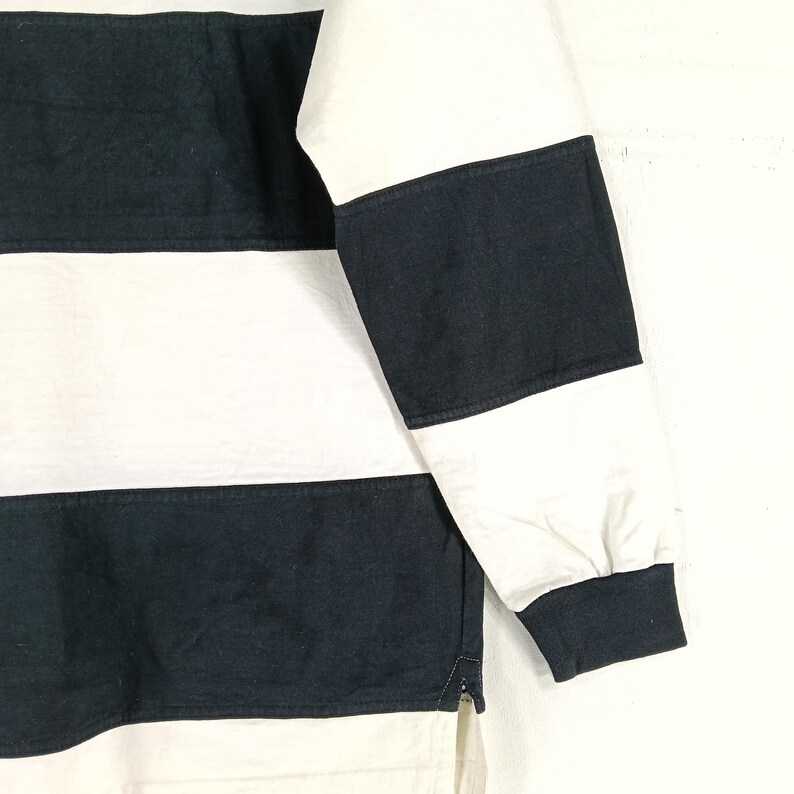 May include: Close-up of a long-sleeved shirt with horizontal stripes. The shirt features alternating wide stripes of navy blue and white. The sleeve cuff and collar are solid navy blue. The shirt is made of a soft, comfortable material.