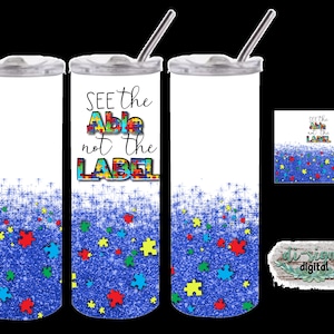 May include: A stainless steel tumbler with a blue glitter background and scattered puzzle pieces. The tumbler has a white lid and a straw. The text "SEE the Able not the LABEL" is printed on the tumbler.