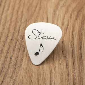 May include: A silver guitar pick with the name "Steve" and a musical note engraved on it.