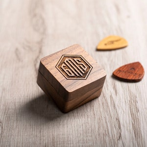 May include: A wooden box with a hexagonal design engraved with the initials "E.M.S." The box is sitting on a light wood surface with two guitar picks beside it.