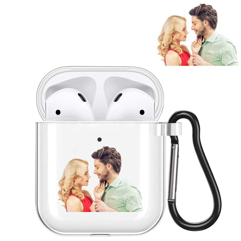 K&ouml;nnte beinhalten: Transparente AirPod-H&uuml;lle mit schwarzem Karabinerhaken. Die H&uuml;lle zeigt ein gedrucktes Bild eines Paares. Die H&uuml;lle ist ge&ouml;ffnet und zeigt wei&szlig;e Airpods im Inneren. Ein zweites Bild des Paares befindet sich in der oberen rechten Ecke.