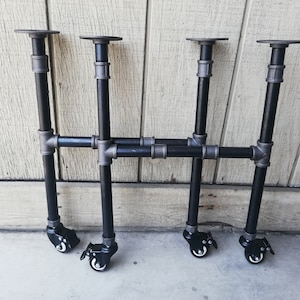 May include: Four black metal table legs with casters. Each leg has a black pipe with a silver fitting at the top and bottom. The legs are connected by two horizontal black pipes.