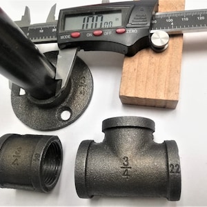 May include: Black iron pipe fittings, including a 3/4 inch tee, a 3/4 inch coupling, and a 3/4 inch flange. The flange is measured with a digital caliper, showing a measurement of 1.00 inches.