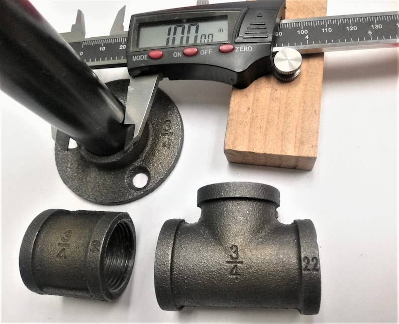 May include: Black iron pipe fittings, including a 3/4 inch tee, a 3/4 inch coupling, and a 3/4 inch flange. The flange is measured with a digital caliper, showing a measurement of 1.00 inches.