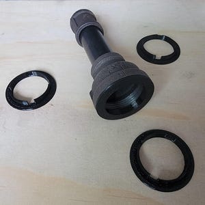 May include: A black metal pipe fitting with three black plastic rings. The pipe fitting has a threaded end and a smooth, cylindrical body. The rings are about 2 inches in diameter and have a small gap in them.