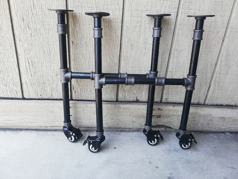 May include: Four black metal table legs with adjustable feet and casters. The legs are made of industrial pipe and have a black finish. The casters are black and have a silver accent.