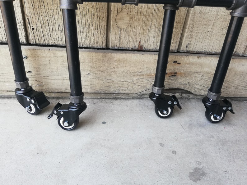 May include: Four black metal legs with black wheels on a concrete surface. The legs are attached to a metal frame.