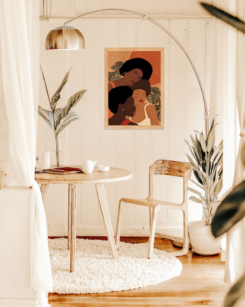 May include: A framed illustration of three women with brown skin, wearing colorful clothing and surrounded by tropical leaves. The illustration is set against a warm orange background.