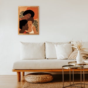 May include: A framed illustration of three women with brown skin tones and short, curly hair. The women are wearing white and red clothing and are surrounded by green leaves. The background is a warm orange color.