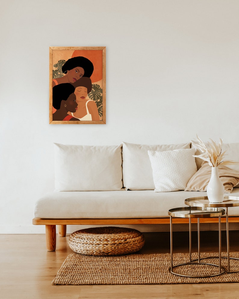 May include: A framed illustration of three women with brown skin tones and short, curly hair. The women are wearing white and red clothing and are surrounded by green leaves. The background is a warm orange color.