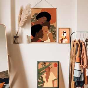 May include: Three framed illustrations of women with brown skin, wearing colorful clothing and surrounded by tropical plants. The illustrations are in a minimalist style with a warm color palette.