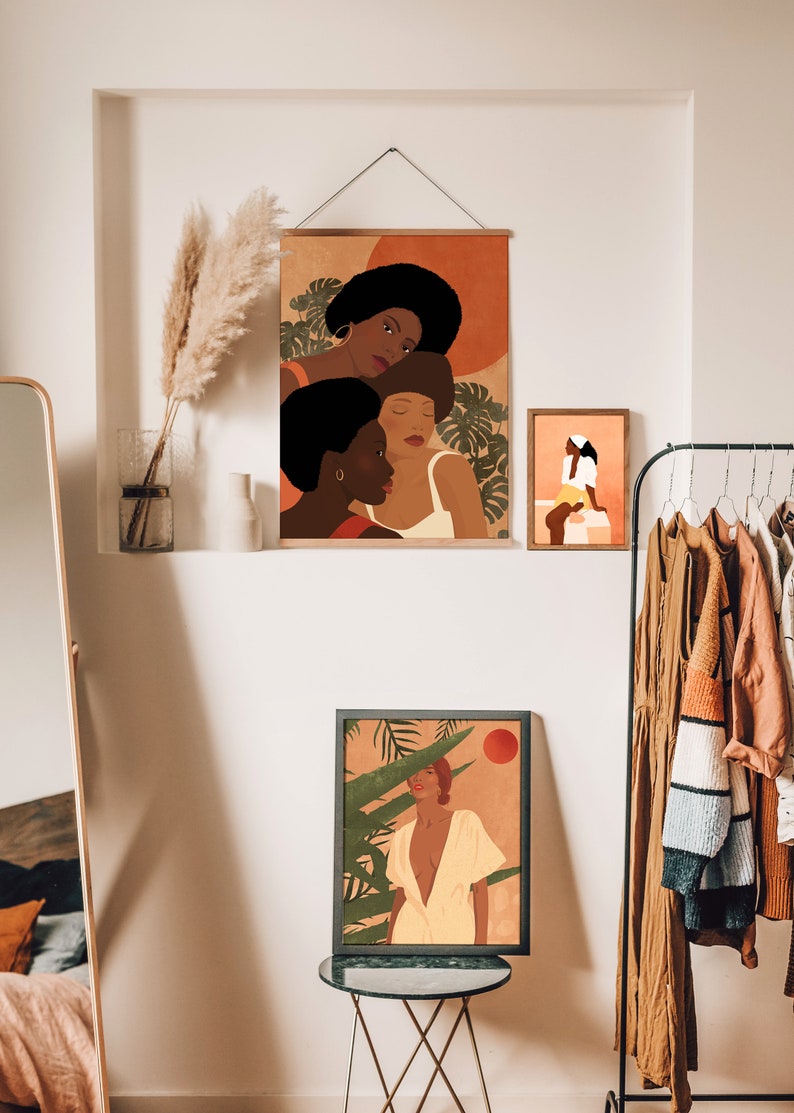 May include: Three framed illustrations of women with brown skin, wearing colorful clothing and surrounded by tropical plants. The illustrations are in a minimalist style with a warm color palette.